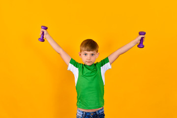 A boy in a green sports shirt holds his hands with dumbbells on the sides, a sports child on a yellow background.
