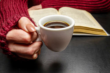 Female hand holds a cup of coffee on the table lies a book