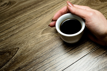 Female hand hugs a cup of coffee on a background of wood table