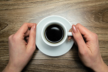 Female hand hugs a cup of coffee on a background of wood table