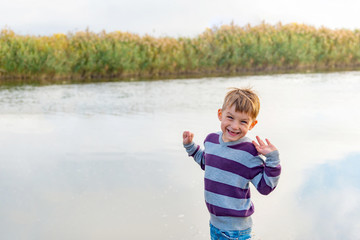 Naklejka premium A joyful and positive child stands on the bank of the river and