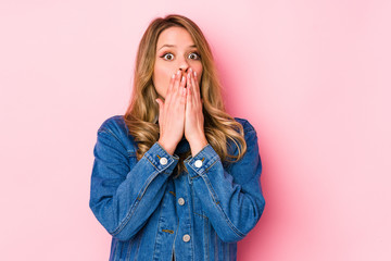 Young caucasian woman isolated on pink background shocked covering mouth with hands.