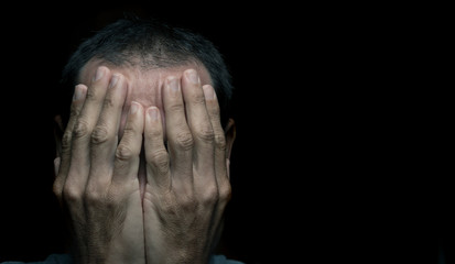 guilty or ashamed  young  man hiding his face  with hand in black background 