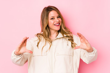 Young caucasian woman isolated on pink background holding something with palms, offering to camera.