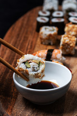 Stock photo of California Roll sushi caught by chopsticks and being introduced into bowl of willow soybeans with more pieces of sushi around.
