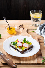 Open sandwich with sliced avocado, radish and lamb's lettuce on a wooden cutting board