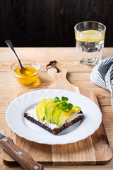 Open sandwich with cream cheese, sliced avocado and lamb's lettuse on a wooden cutting board