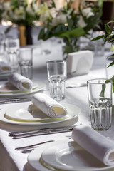 Festive table with a white tablecloth. Served with dishes, glasses and lush bouquets. Wedding table. Table decoration
