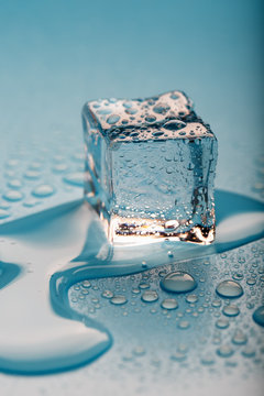 Naklejki Ice cube with water drops on a blue background. The ice is melting.