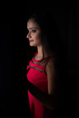 Fashion portrait of an young and attractive Indian Bengali brunette girl in pink western dress looking through  a window in dark background. Indian fashion portrait and lifestyle.