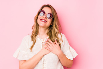 Young caucian woman with glasses isolated on pink background laughing keeping hands on heart, concept of happiness.