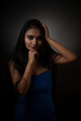 Obraz premium Fashion portrait of an young and attractive Indian Bengali brunette girl with blue western dress in front of a black studio background. Indian fashion portrait and lifestyle.