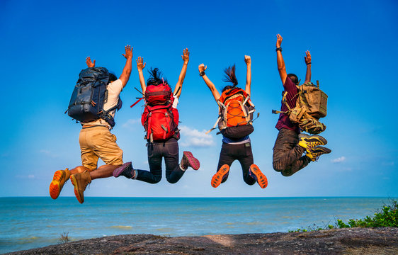 Group of people jumping on mountain top cliff edge. Happy traveler jumping with backpack travel lifestyle adventure concept. Active summer vacations outdoor on mountains success and fun