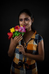 Fashion portrait of an young and attractive Indian Bengali brunette girl in checkered western dress with vibrant flowers in front of a black studio background. Indian fashion portrait and lifestyle.
