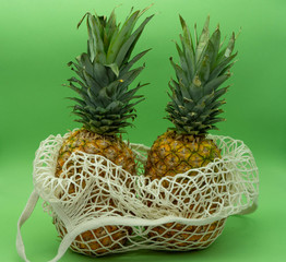 Two pineapples in insulated organic cotton bags on a green background. Healthy and ecological food concept. Zero waste.