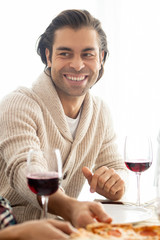 Positive handsome mixed race man with stubble sitting at table with wineglasses and chatting with friends at dinner party