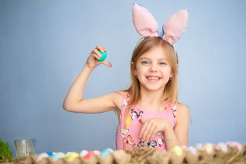 Cute little baby wears bunny ears on Easter day. cute little girl holding easter eggs in her hands and smiling. blue background