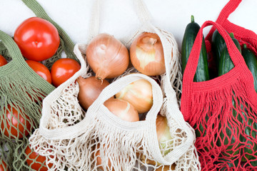 White, green and red mesh shopping bag with red tomatoes, bow and green cucumbers on white background.