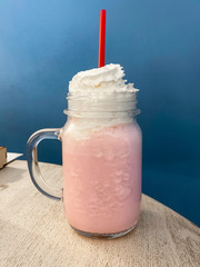 strawberry smoothie in a glass jar with whipped cream and red straws on a rustic table and blue wall background. Strawberry Flavored Milk Shake