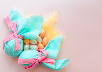 Egg gift in green paper packaging and with pink ribbon Easter Bunny wrap idea. Chocolate dragee white and gold color, multicolor colorful feathers. Minimal concept. Flat lay, Copy space, top view