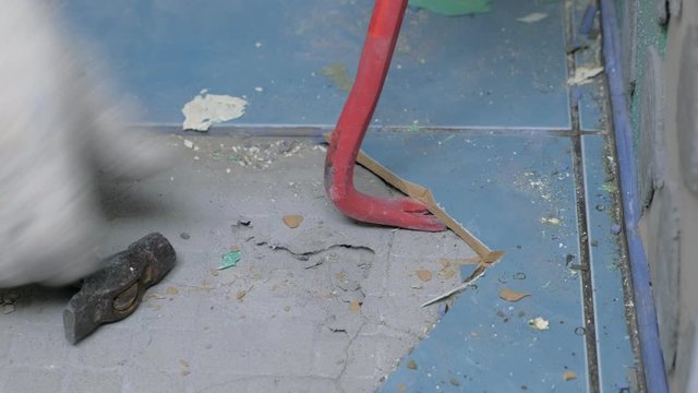 Tiler making renovation, removing tiles from floor in toilet using tools crowbar, hammer and spatula, hands closeup. Construction works. Unrecognizable builder wearing in uniform and gloves.