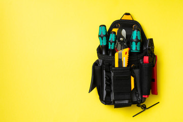 Black electrician installer's bag with tools on a yellow background