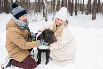 Cheerful young man and woman spending time together with their dog outdoors of winter day, horizontal shot