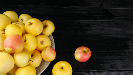 Ripe yellow apples in a ceramic plate on a black wooden table. Place for text.