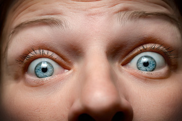 Close-up face of caucasian woman with blue eyes expressing fear and surprise with horror