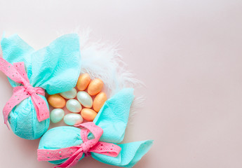 Egg gift in green paper packaging and with pink ribbon Easter Bunny wrap idea. Chocolate dragee white and gold color, multicolor colorful feathers. Minimal concept. Flat lay, Copy space, top view