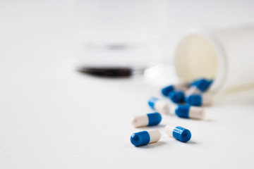 Pile of blue-white capsules and glass of water on white table. Course of treatment. Copy space.