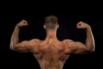 powerful muscular athlete shows off his back beside black wall