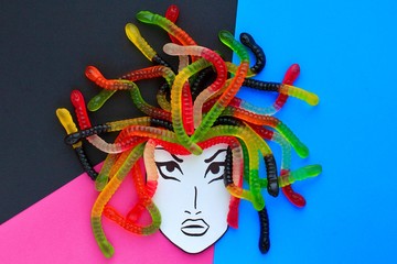 Jelly worms or snakes candies lying like a woman's or a Gorgon's Medusa hair on a multicolored background. Creative concept of food, sweets.