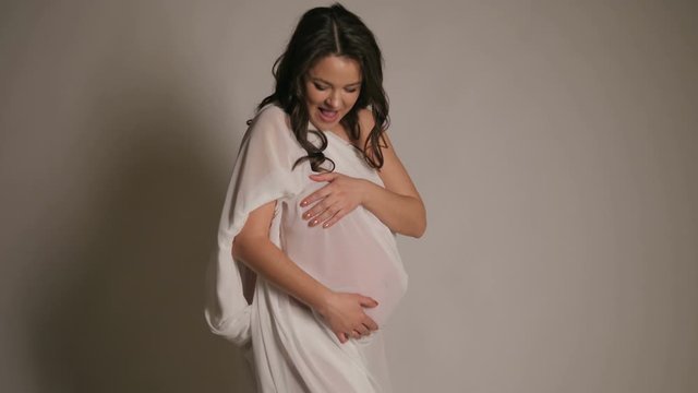 Portrait of a happy laughing naked pregnant woman in the Studio on a white background, she is wrapped in a white silk fabric.
