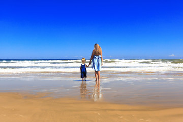 Mom and daughter are walking on the beach. Back view, copy space.