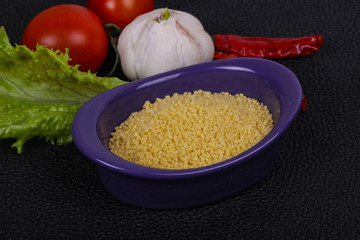 Raw couscous in the bowl served salad leaves, tomato and pepper