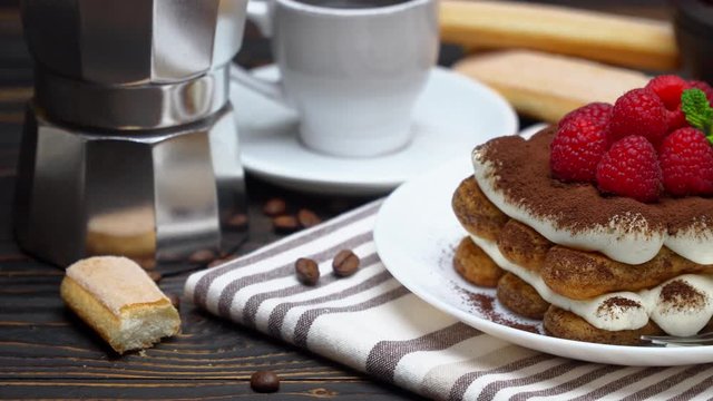 portion of tiramisu dessert with raspberries cup of espresso and coffee maker on wooden background