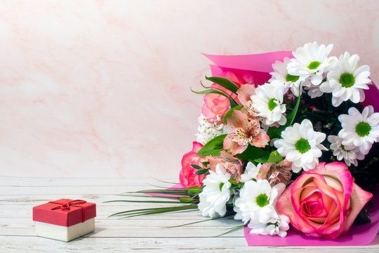 Romantic background with a bouquet of colorful flowers and a gift box on pink. Side view with copy space. Mother's Day, Women's Day background.