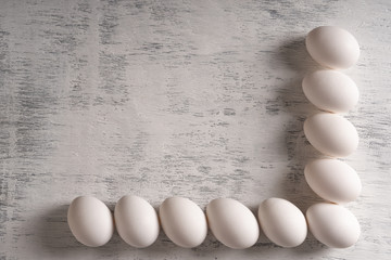 Light wooden surface with a frame of white eggs. The view from the top, flat lay.