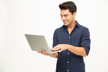 Portrait of an excited man holding laptop computer and celebrating success over white background,...