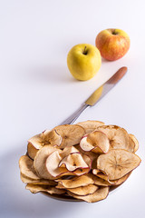 Dried apple fruit chips in a plate on foreground and fresh apples on background.