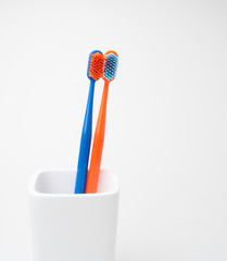Two colored toothbrushes, blue and orange, for oral care, in a white toothbrush holder on a white background
