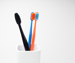 Three toothbrushes, black, blue and orange, for oral care, in a white toothbrush holder on a white background
