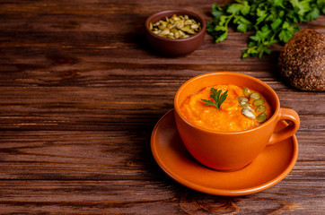 Vegetarian autumn cream soup of pumpkins and carrots with seeds and parsley on a wooden background with copy space, flat lay