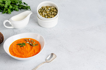 Vegetarian autumn cream soup of pumpkins and carrots with seeds and parsley on a gray background with copy space, flat lay