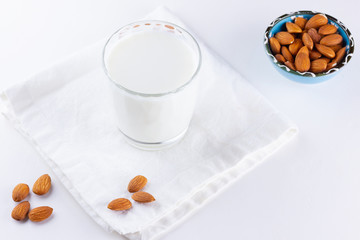 Almond milk with almond on white background. Organic almond milk in a glass for healthy breakfast. Vegan milk from almonds nuts on a white napkin. Alternative milk