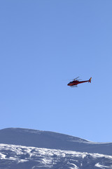 Fototapeta na wymiar Helicopter in blue clear sky and snowy ski slope