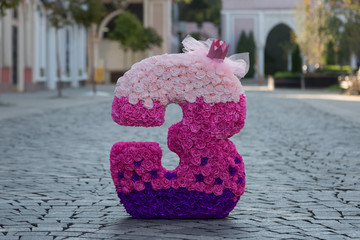 Pink number three. The figure is covered with paper flowers. The concept of a girl's birthday.