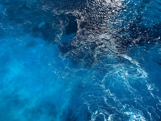 Natural blue background. Blue surface of sea water with wave and foam. Texture of blue water. Abstract textured backdrop. Horizontal, blur, cropped shot, free space for text. Concept of natural beauty