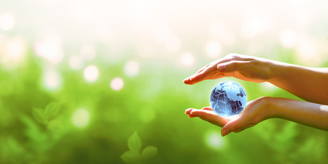 Card for World Earth Day. Blue planet crystal glass globe ball in human hand on blurred green background. Saving environment, save, protect clean planet and ecology, sustainable lifestyle concept.